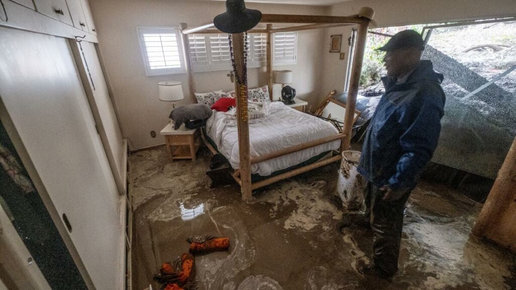 Flooded bedroom with muddy floor and man standing.
