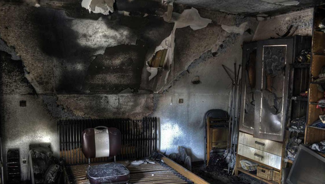 Burnt room with charred walls and damaged furniture.